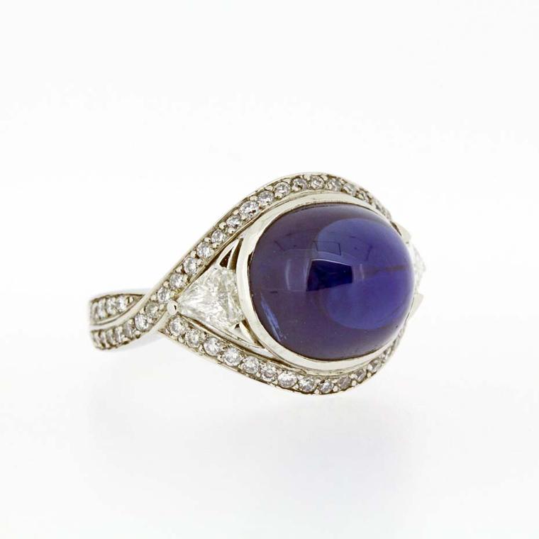 A unique sapphire engagement ring from Brighton-based Baroque Jewellery in white gold set with a large blue cabochon sapphire, flanked by trillion-cut diamonds with grain-set diamonds on the shank.